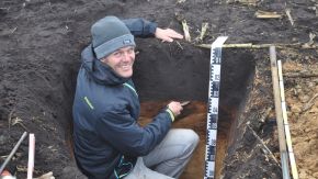 Ein Amtsmitarbeiter erstellt ein Bodenprofil. Dazu misst er knieend die Tiefe einer Grube aus. Es muss akkurat ein Meter ausgehoben werden. (Quelle: Maxime Nauche, LfU) Ein Amtsmitarbeiter erstellt ein Bodenprofil. Dazu misst er knieend die Tiefe einer Grube aus. Es muss akkurat ein Meter ausgehoben werden.